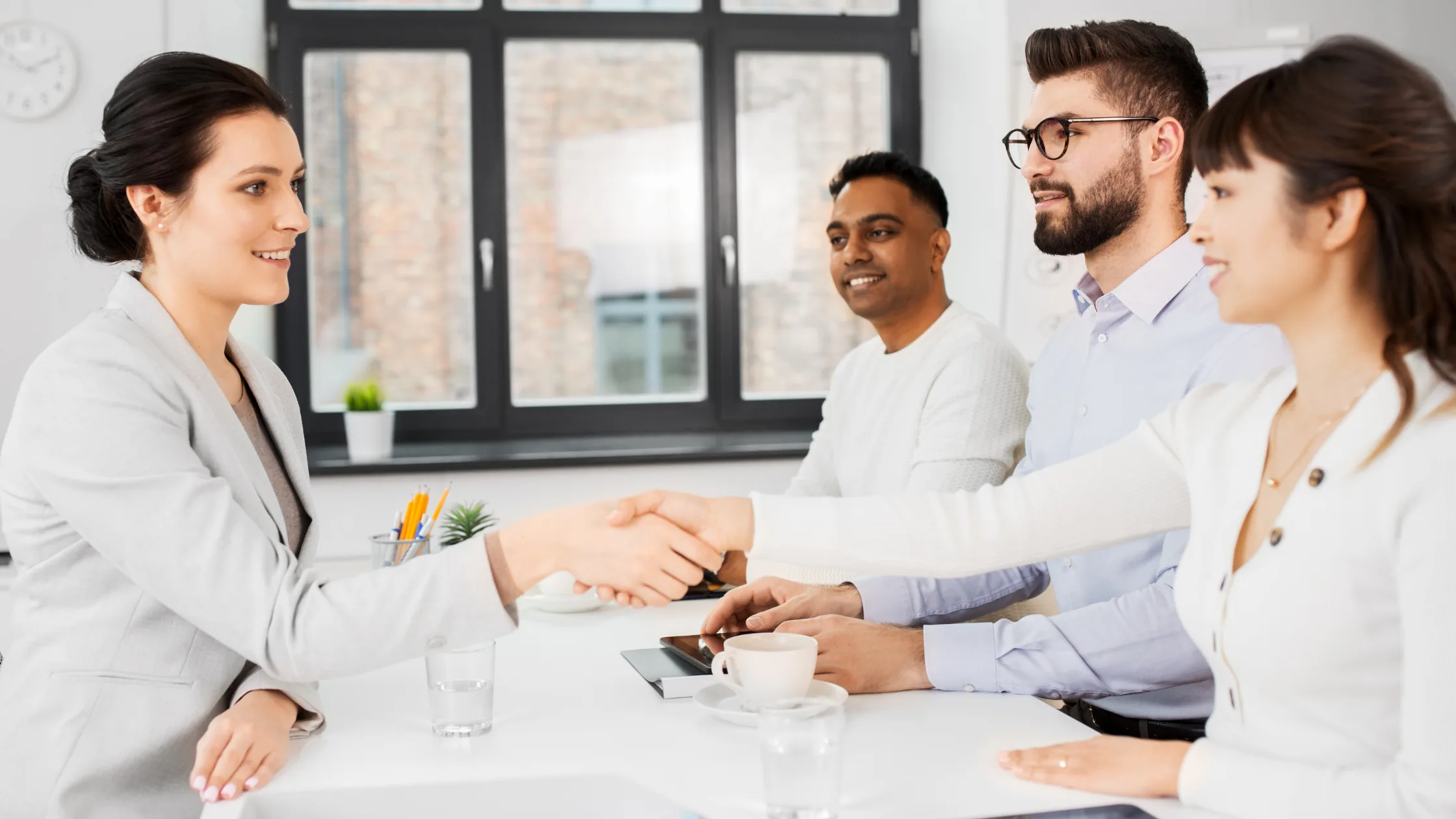 two women shaking hands at a table during a business meeting with two men.